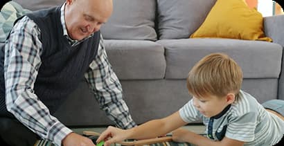 Adulto mayor y niño juegan juntos en el suelo de la sala.