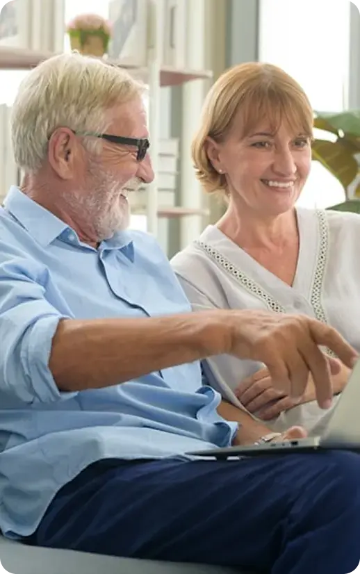 Pareja de adultos mayores sonríe mientras utiliza una computadora portátil en casa.